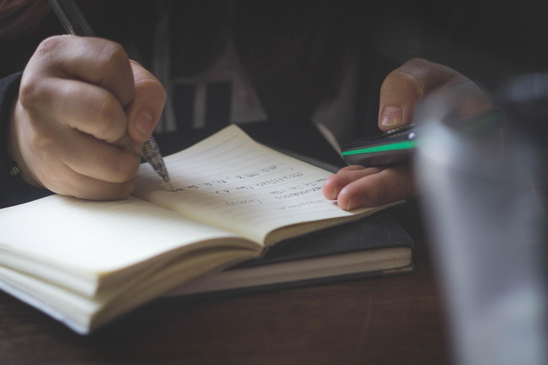 Iemand die tekst in een boekje schrijft met een pen